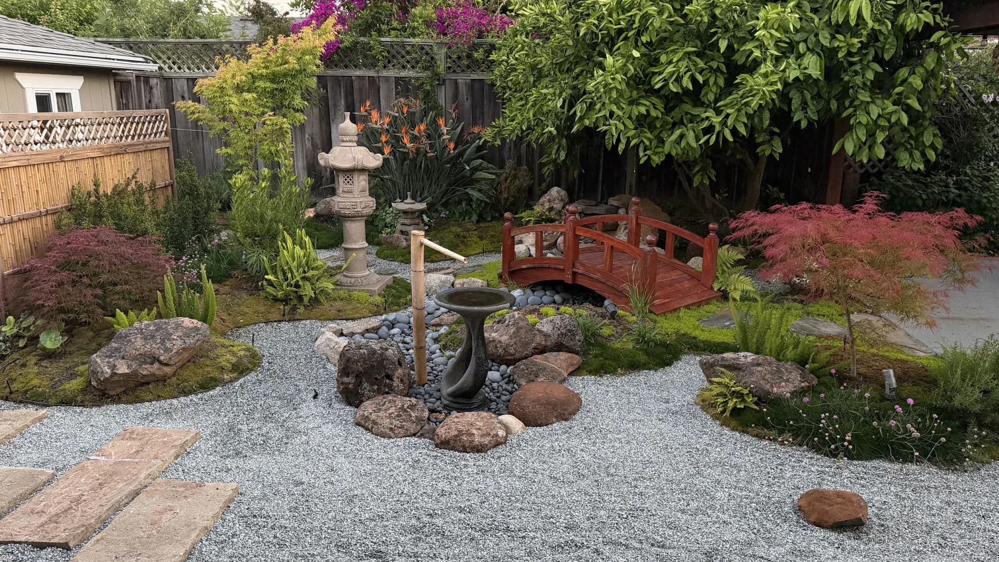 After: Japanese-inspired garden with a red timber bridge, stone lanterns, gravel paths and layered planting